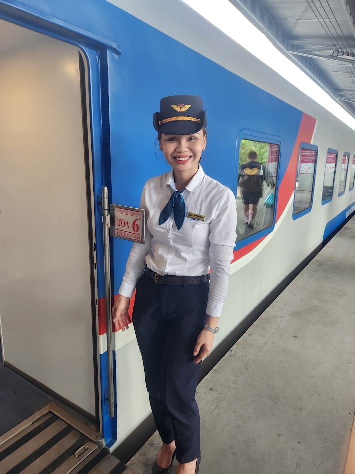 A Vietnamese train attendant smiling at the door of Car 6